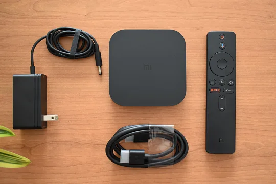 L'image montre ce qui est inclus dans la boîte Xiaomi Mi Box S 4K : la boîte tv, la télécommande, le câble HDMI et un chargeur.