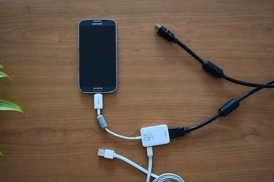 La photo montre un téléphone Samsung connecté à un adaptateur MHL / HDMI. Un câble HDMI et le câble USB du téléphone sont connectés à l'adaptateur.